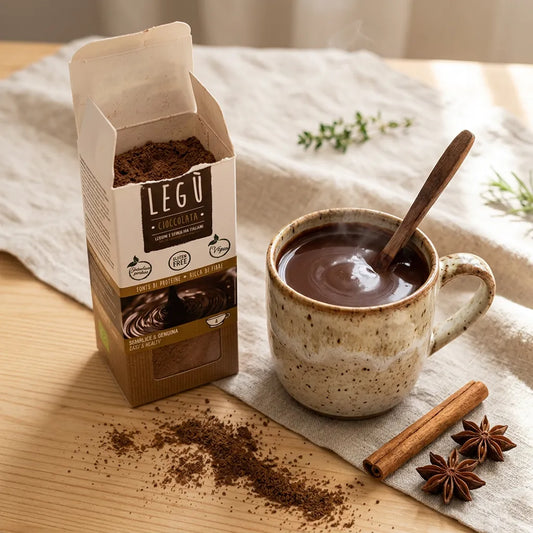 Mix cioccolata calda LEGÙ, una tazza di cioccolata fumante con cucchiaio di legno, una scatola aperta del mix, spezie e polvere di cacao, con evidenza di legumi, senza glutine e ad alto contenuto di proteine vegetali.