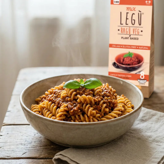 Piatto di fusilli LEGÙ caldi e fumanti conditi con Ragù Veg di legumi, guarniti con fogliolina di basilico. Sullo sfondo, confezione del Ragù Veg, senza glutine e ricco di proteine.