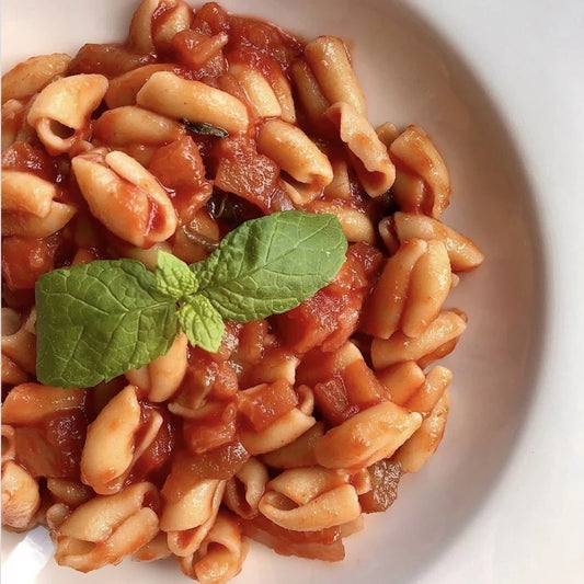 Chicche LEGÙ 4 Legumi (fagioli bianchi, ceci, lenticchie gialle, piselli gialli) cotte, in un piatto bianco, condite con salsa di pomodoro e una foglia di menta. Piatto perfetto con proteine vegetali e naturalmente senza glutine.