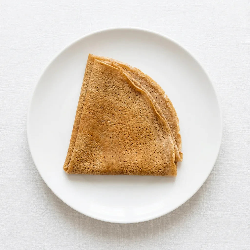 Una crepe sottile e dorata, preparata con farina di sorgo LEGÙ, piegata a spicchio su un piatto bianco. Perfetta per ricette senza glutine e proteine vegetali.