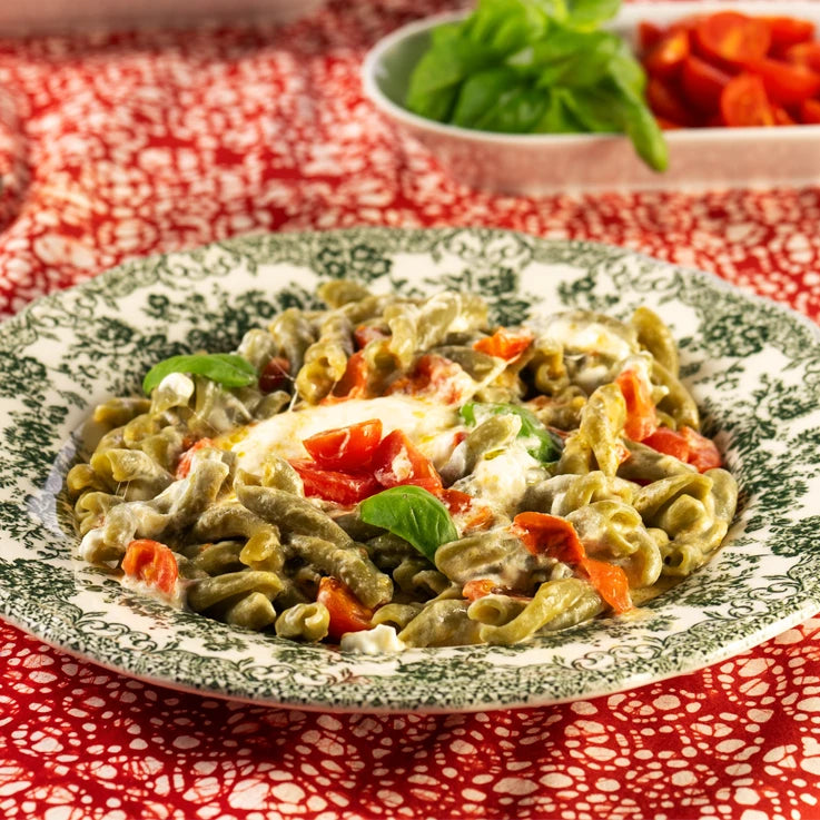 Un piatto pronto di Intrecci ÙNICA LEGÙ (mais, piselli e spirulina 100% italiani), pasta di legumi senza glutine, condita con pomodorini e basilico, con alto contenuto di proteine vegetali.