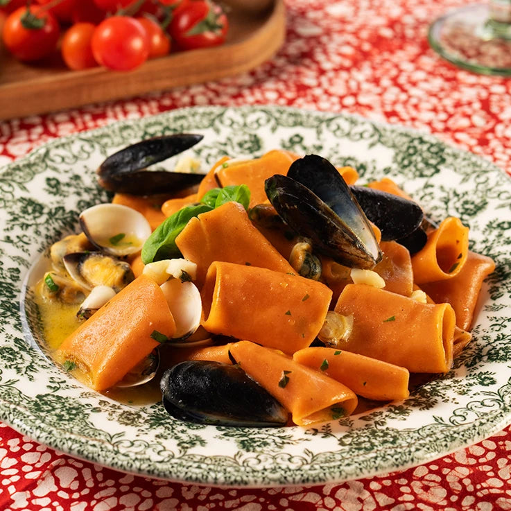 Piatto di Paccheri ÙNICA LEGÙ con mais, lenticchie rosse e pomodoro, senza glutine, cucinati con frutti di mare e basilico, fonte di proteine vegetali.