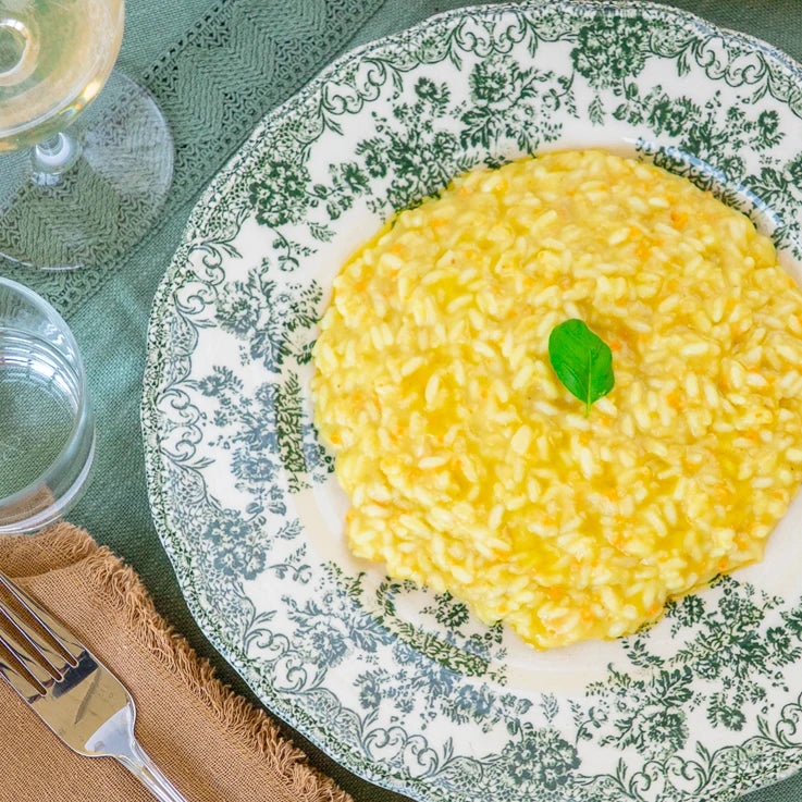 Piatto di riso cremoso con carote, zucchine e basilico, con bicchiere d'acqua e vino.